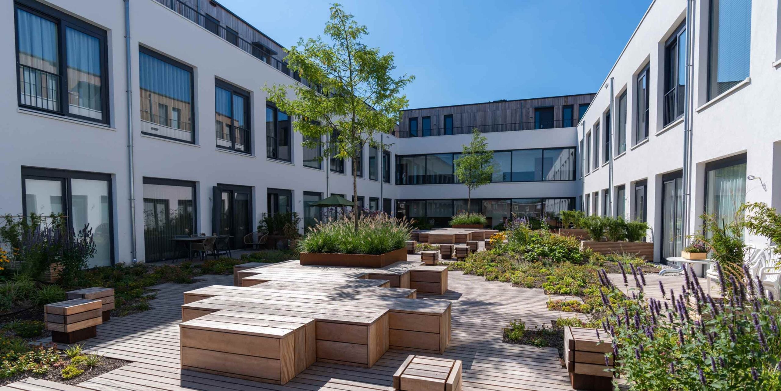 Ingerichte binnentuin bij appartementencomplex met houten terrasdek, zitelementen en beplanting.
