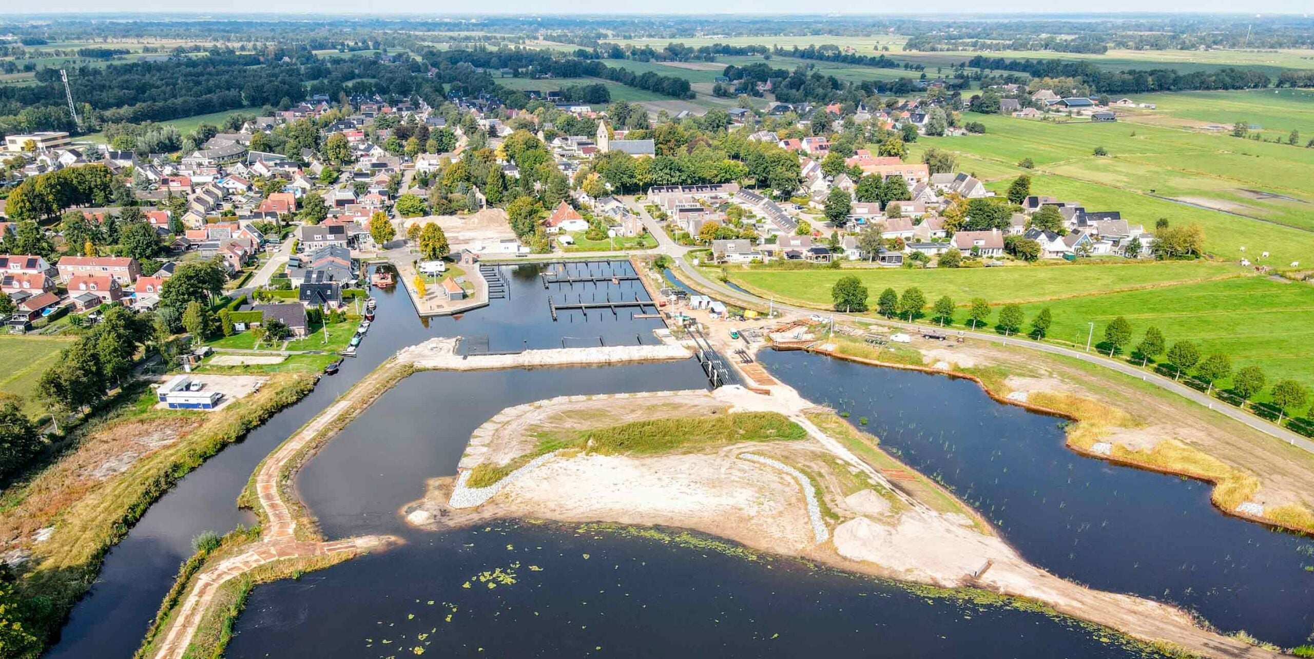 Luchtfoto van een dorp met jachthaven en heringerichte waterpartij met nieuw aangelegde oevers.
