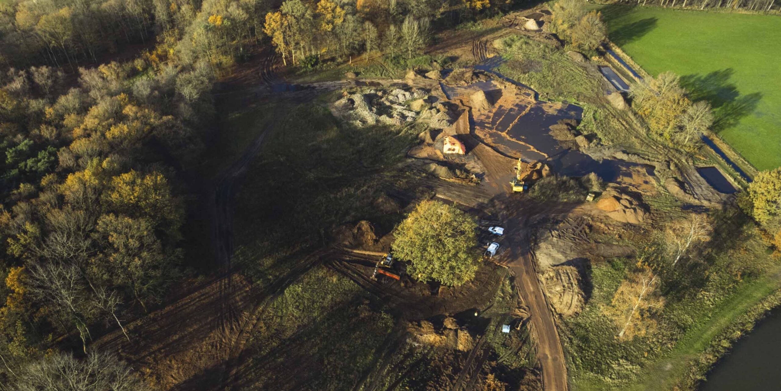 Luchtfoto van grondwerkzaamheden met graafmachines in bosgebied bij aanleg van waterpartij.