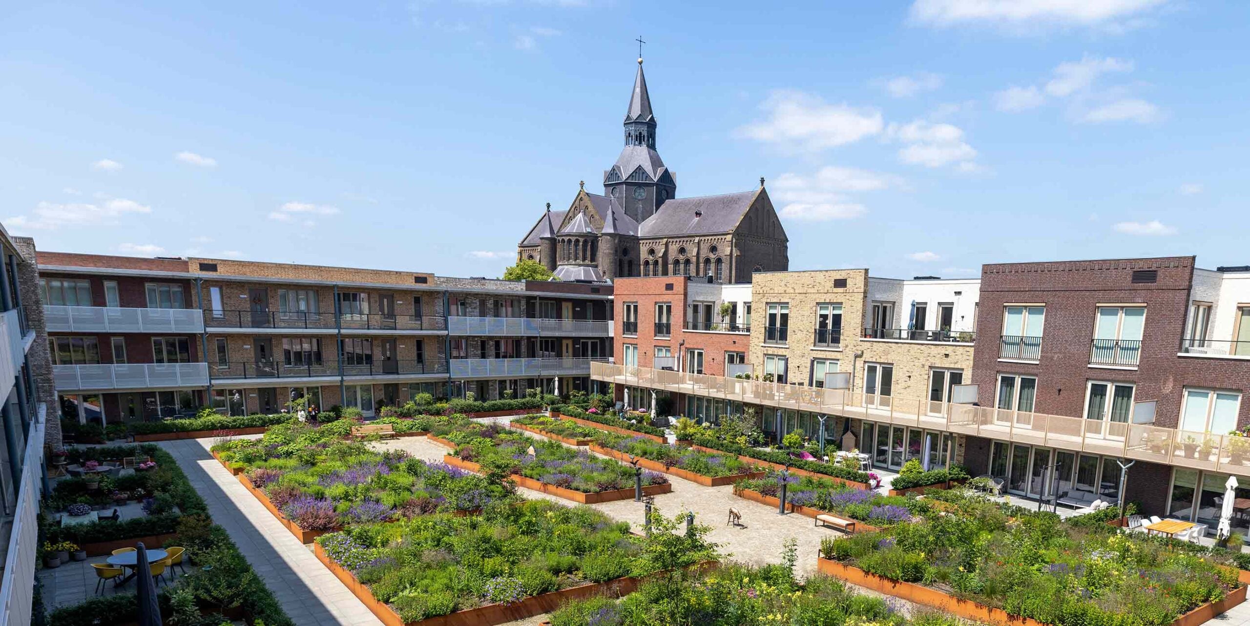 Beplante binnentuin met cortenstalen plantenbakken tussen woningen, met kerktoren op de achtergrond.