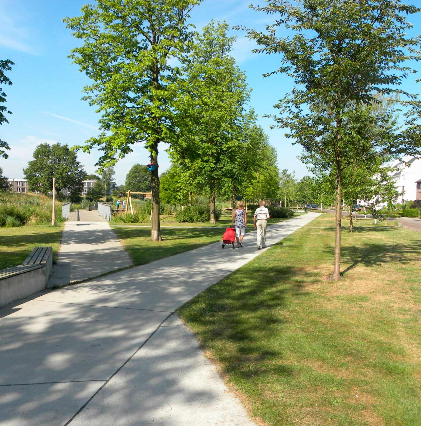 Wandelpad door groen wijkpark met bomen, gazon en speeltuin in woonwijk.
