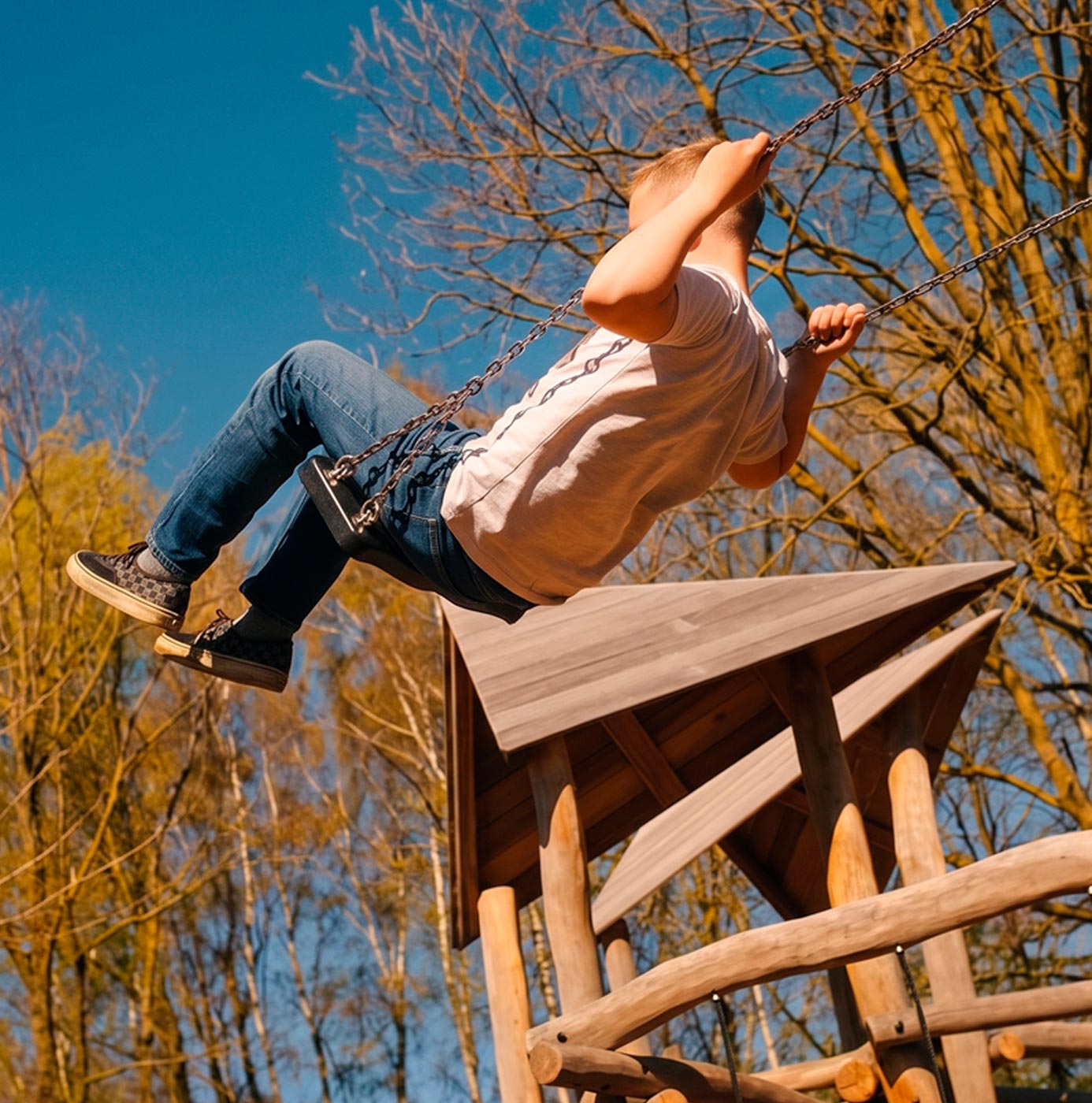 Kind schommelt hoog op speeltoestel bij een houten speelhuisje in een groene speeltuin.