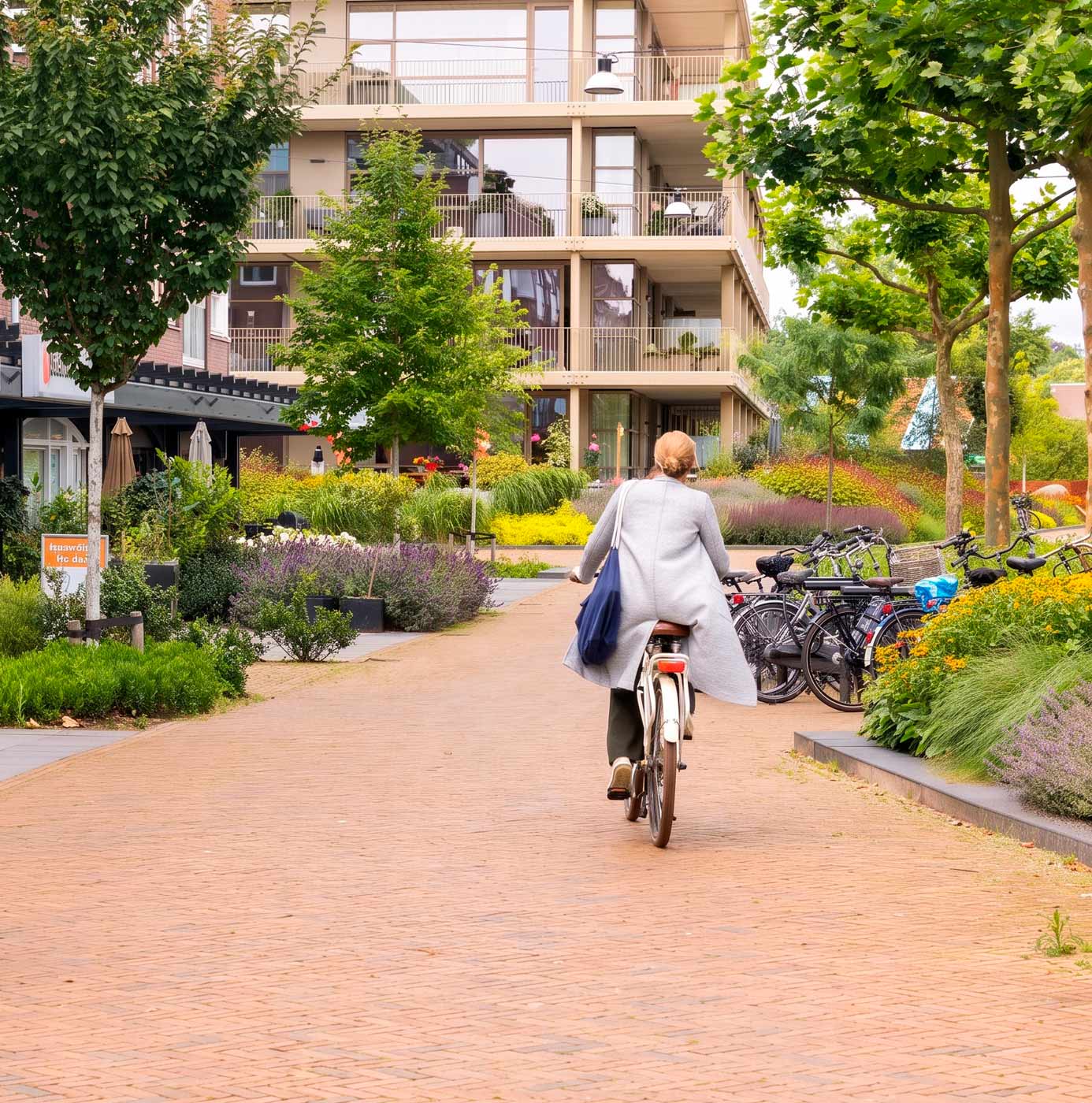 Fietser rijdt over een verhard pad langs beplante groenstroken tussen appartementen in een woonwijk.
