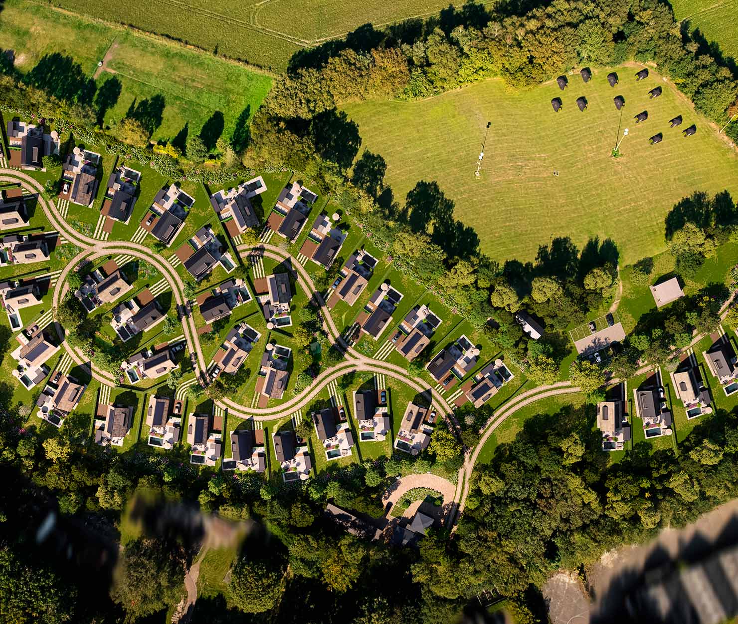 Luchtfoto van een woonwijk met groene tuinen, slingerende paden en aangrenzend grasland.