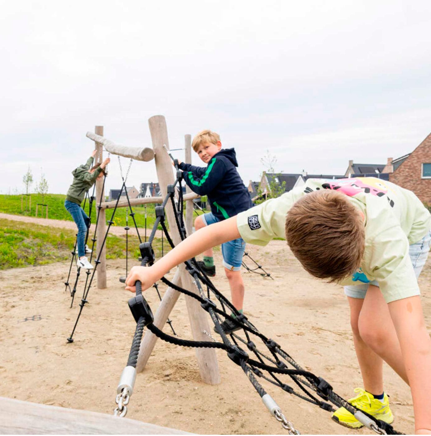 Kinderen klimmen op een houten klimtoestel met touwnetten op een speelplek in een woonwijk.