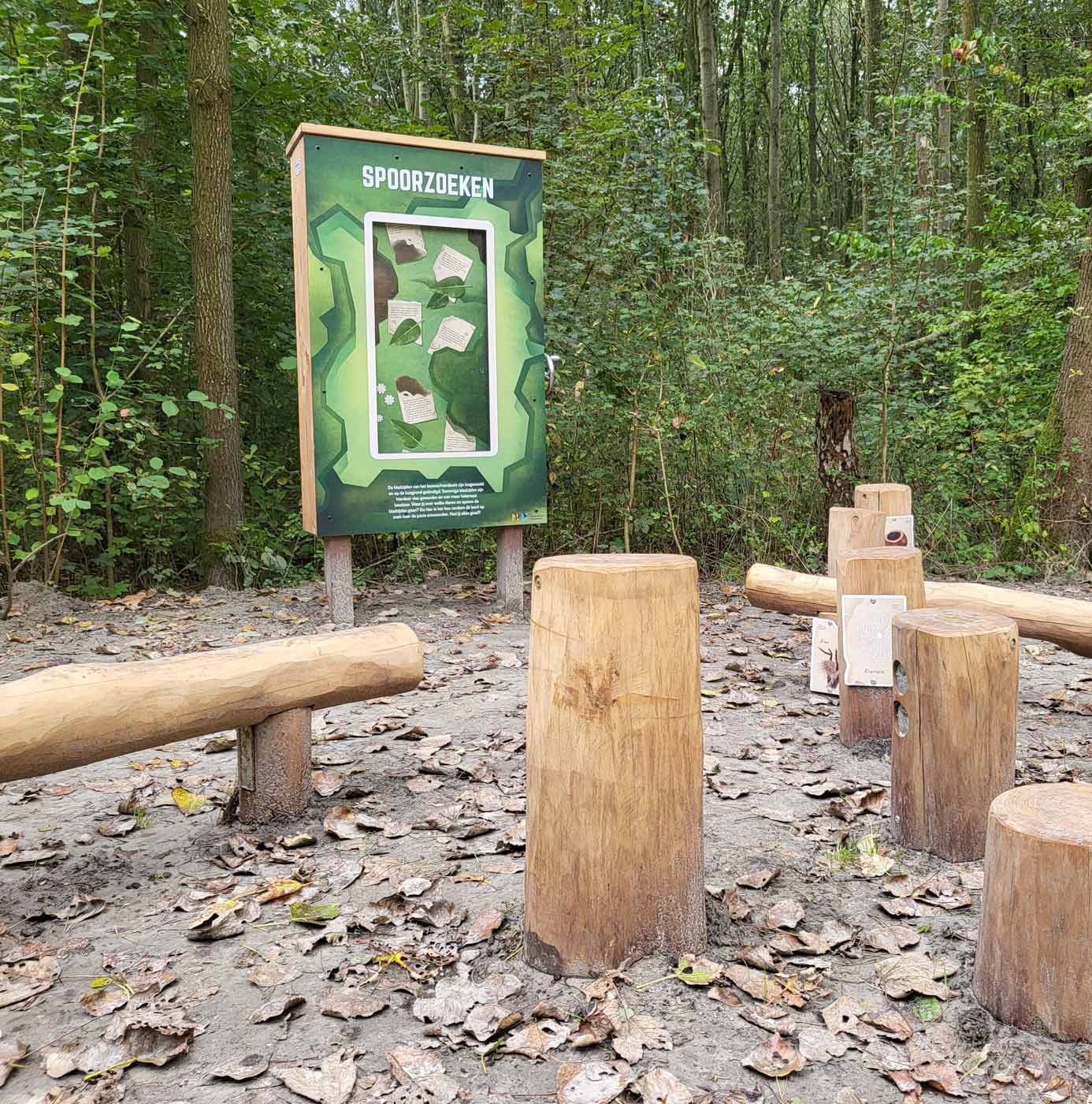 Speel- en informatiepunt 'Spoorzoeken' in het bos met houten boomstammen en informatiebord.