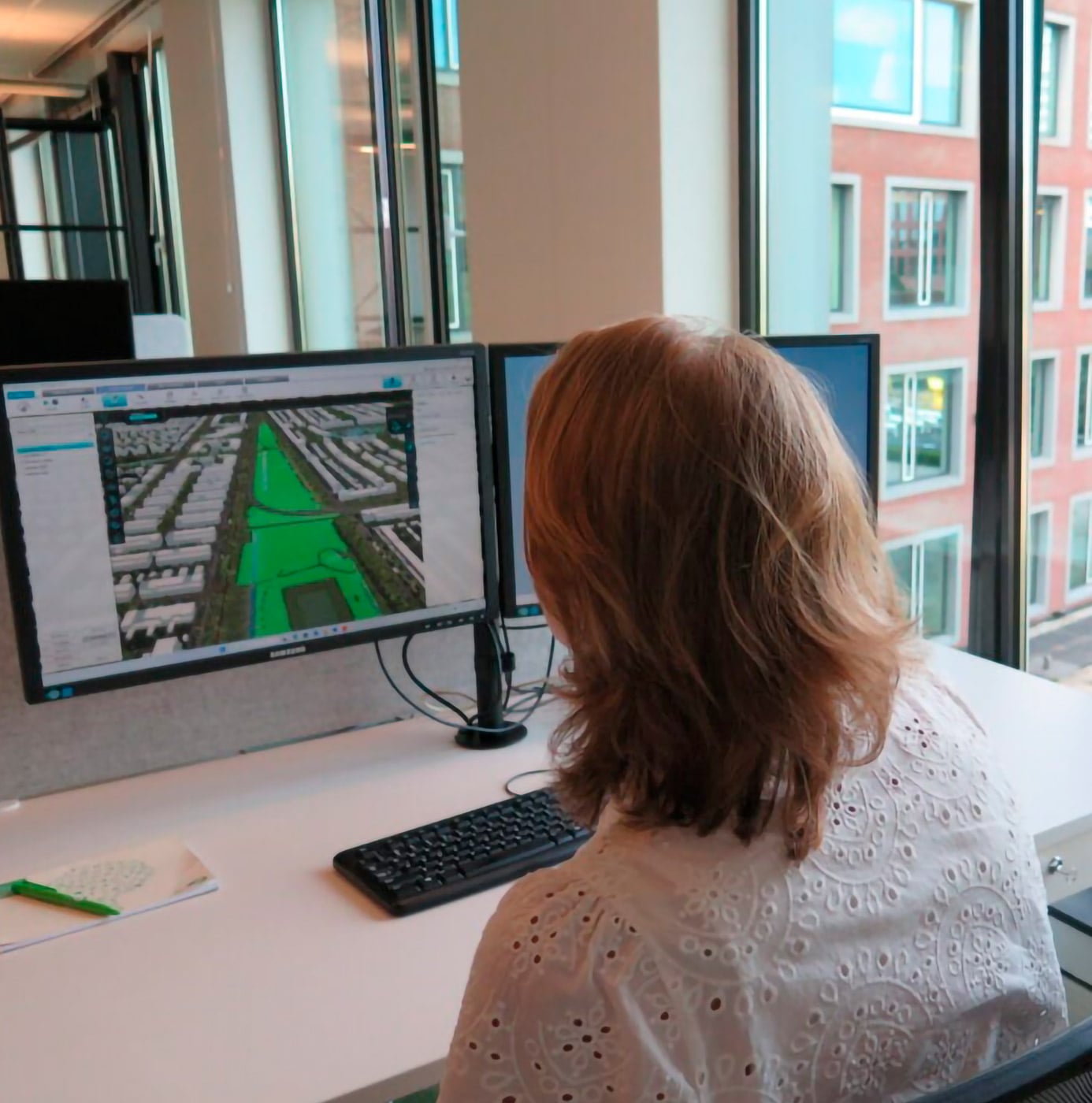 Medewerker analyseert een groenplan van een woonwijk op meerdere beeldschermen op kantoor.