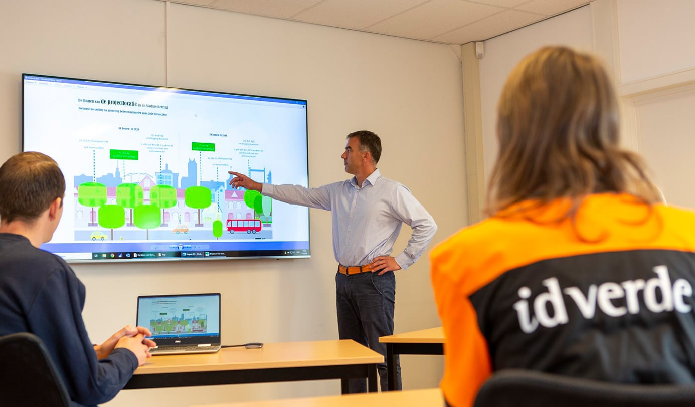 Medewerker geeft toelichting op boombeheerplan bij scherm tijdens overleg met idverde-collega's.