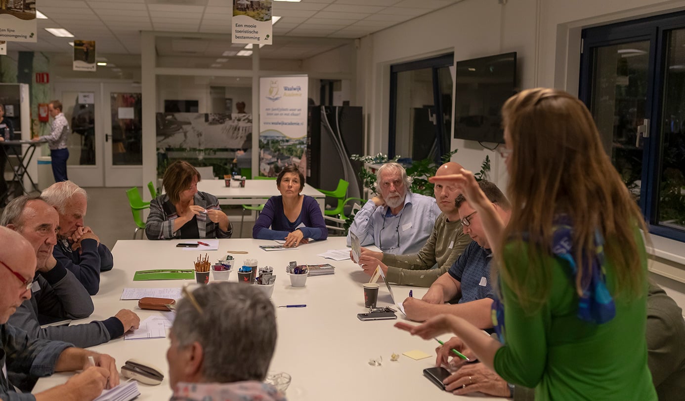 Deelnemers luisteren tijdens een informatiebijeenkomst over groenbeheer aan een ronde tafel.