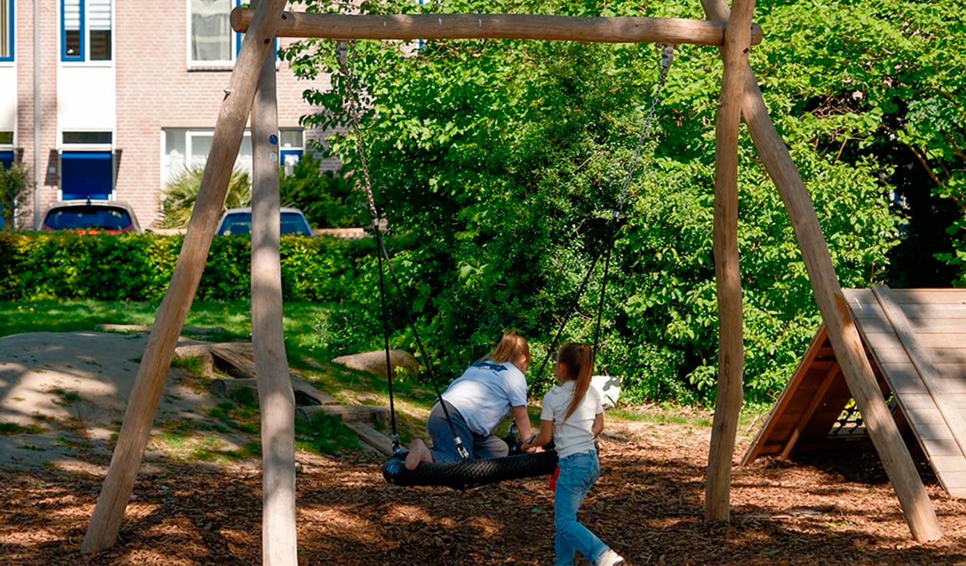 Kinderen spelen op een houten schommel in een groene speeltuin bij een woonwijk.