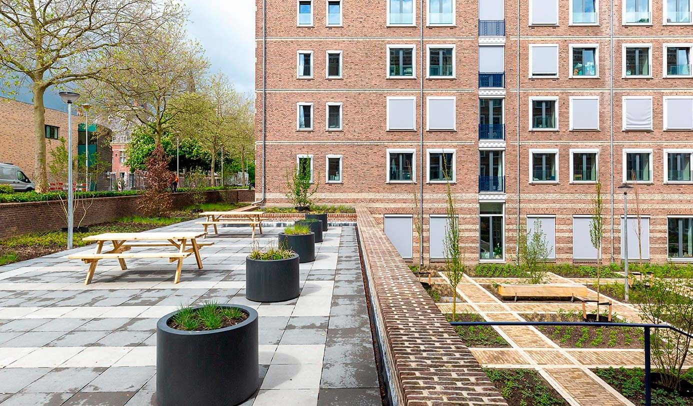 Ingerichte binnentuin bij appartementencomplex met picknicktafels, plantenbakken en verhoogde plantvakken.