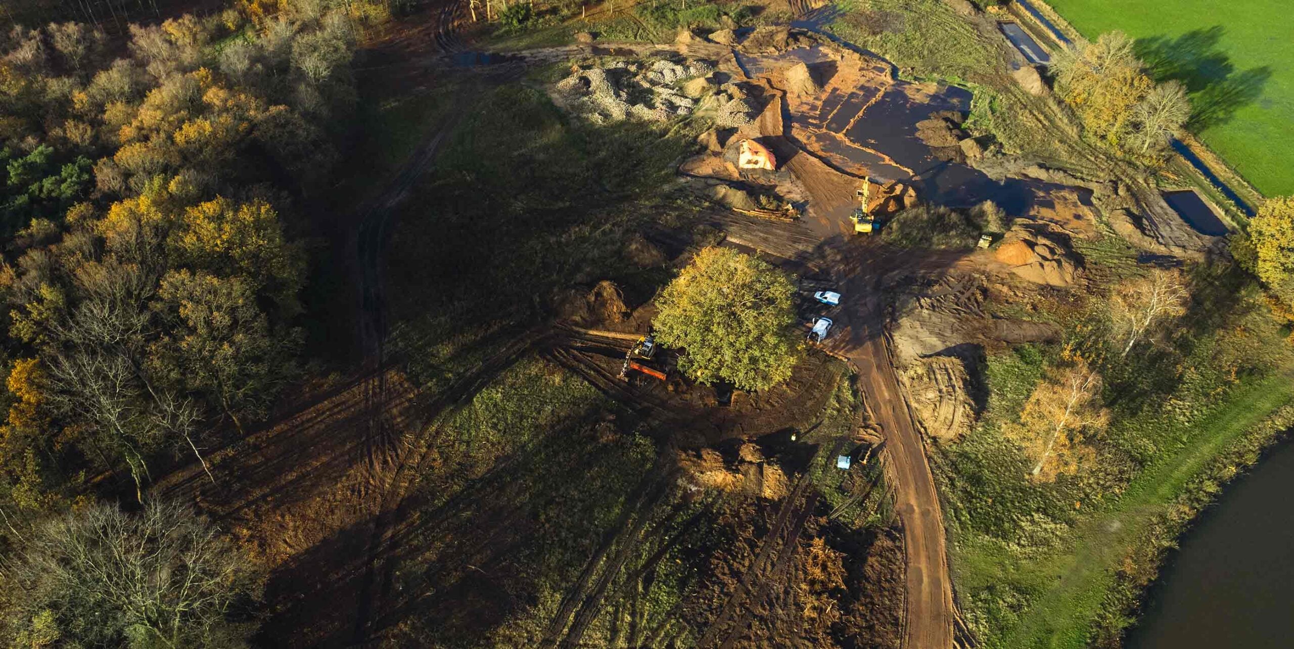 Luchtfoto van grondwerkzaamheden met graafmachines in een bosrijk landschap.