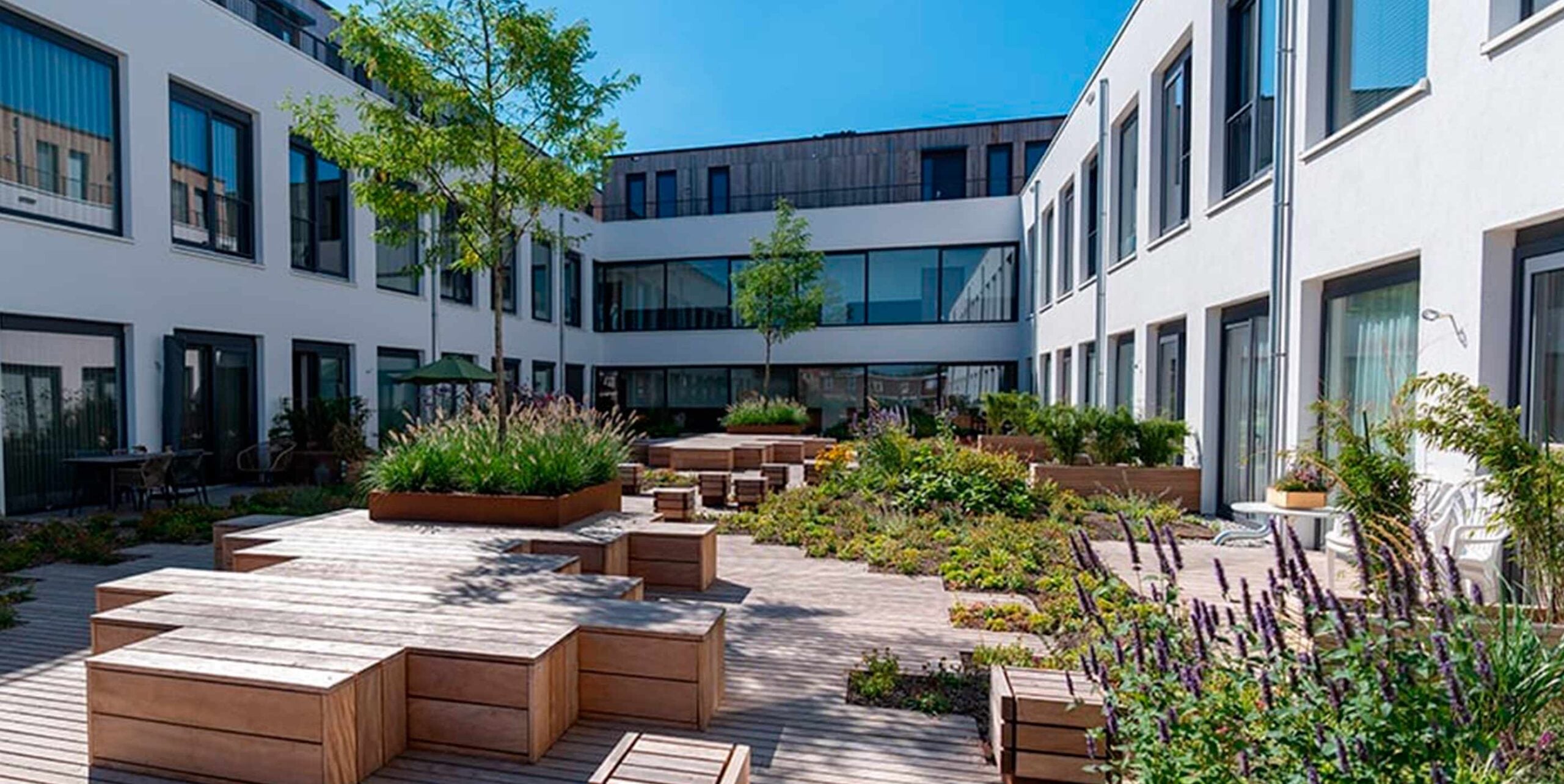 Groene binnentuin met houten terrassen en beplanting tussen appartementengebouwen.
