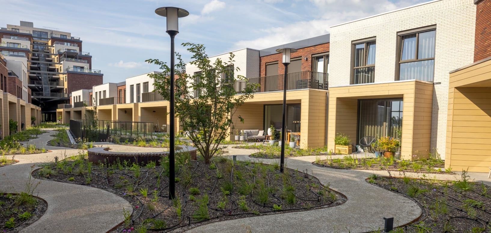 Groene binnentuin met slingerende paden en jonge beplanting tussen nieuwbouwwoningen.