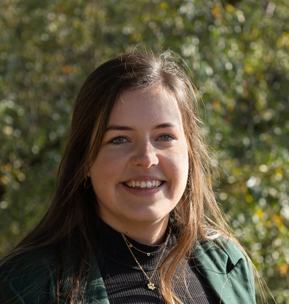 Anouk Gloudemans, adviseur Engineering & Contracten bij idverde, lachend voor de camera met groen gebladerte op de achtergrond.