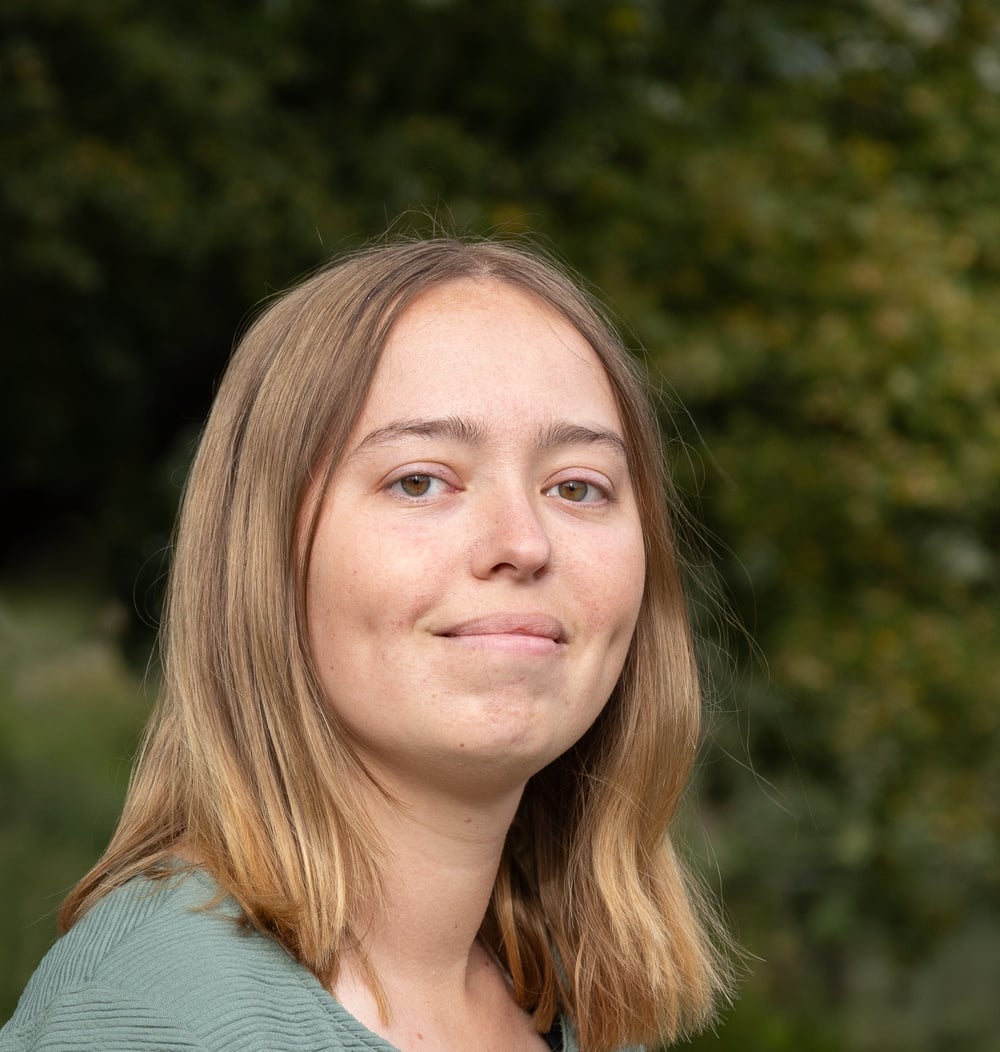 Anouk van der Palen, adviseur Strategie & Beleid bij idverde, buiten met groene begroeiing op de achtergrond.