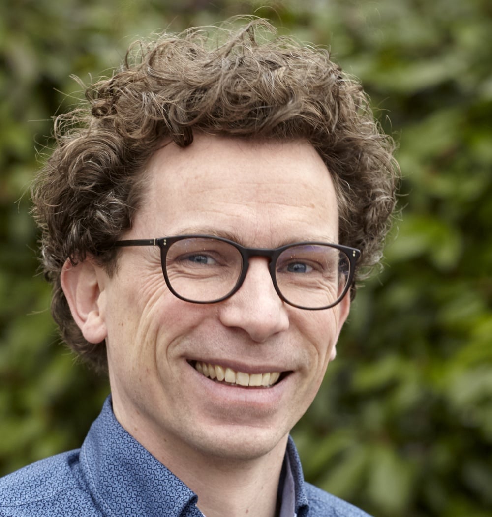 Arjan Schoenmakers, teamleider Ecologie bij idverde, glimlachend voor een groene heg.