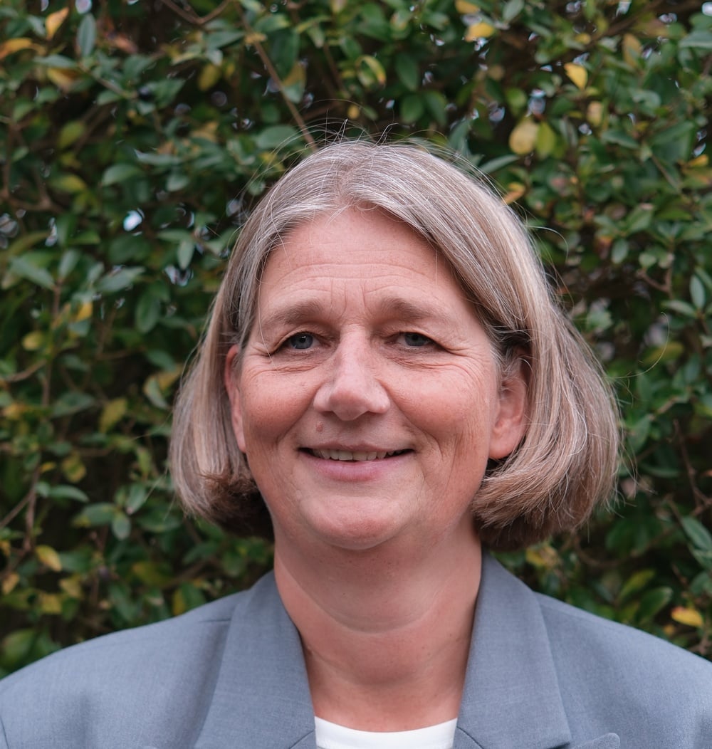 Bianca Senssen, KAM Coördinator bij idverde, glimlacht voor een groene heg.