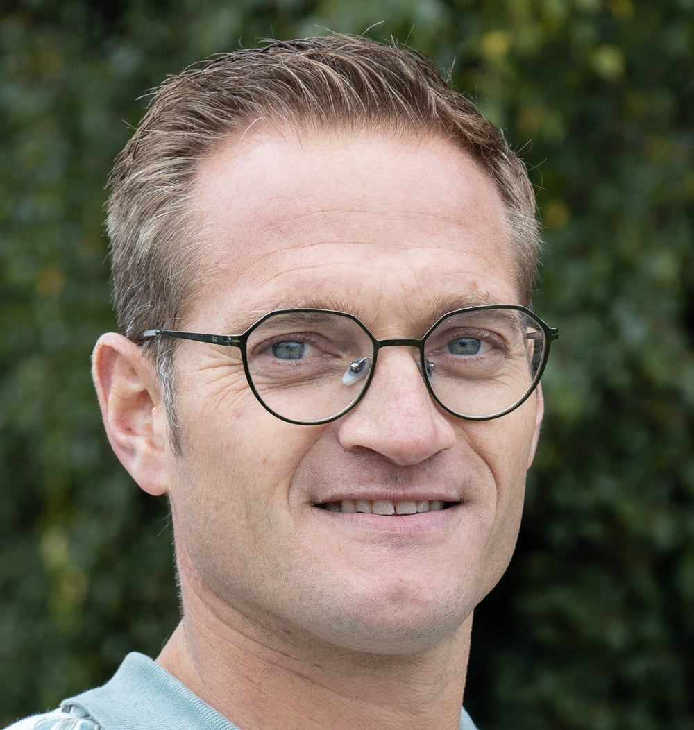 Corné den Otter, senior projectleider bij idverde, portretfoto met groene beplanting op de achtergrond.