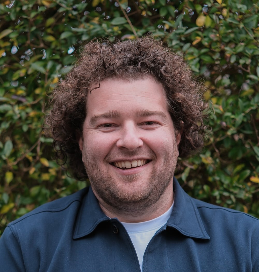 Dennis van Kempen, vestigingsmanager bij idverde, lachend voor een groene heg.