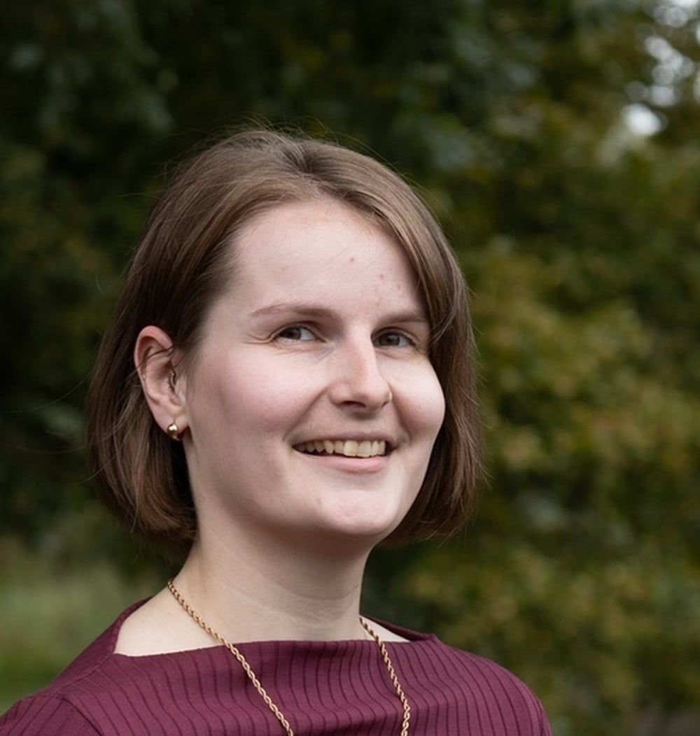 Medewerker Dionne Visch, adviseur ecologie, portretfoto met groene begroeiing op de achtergrond.