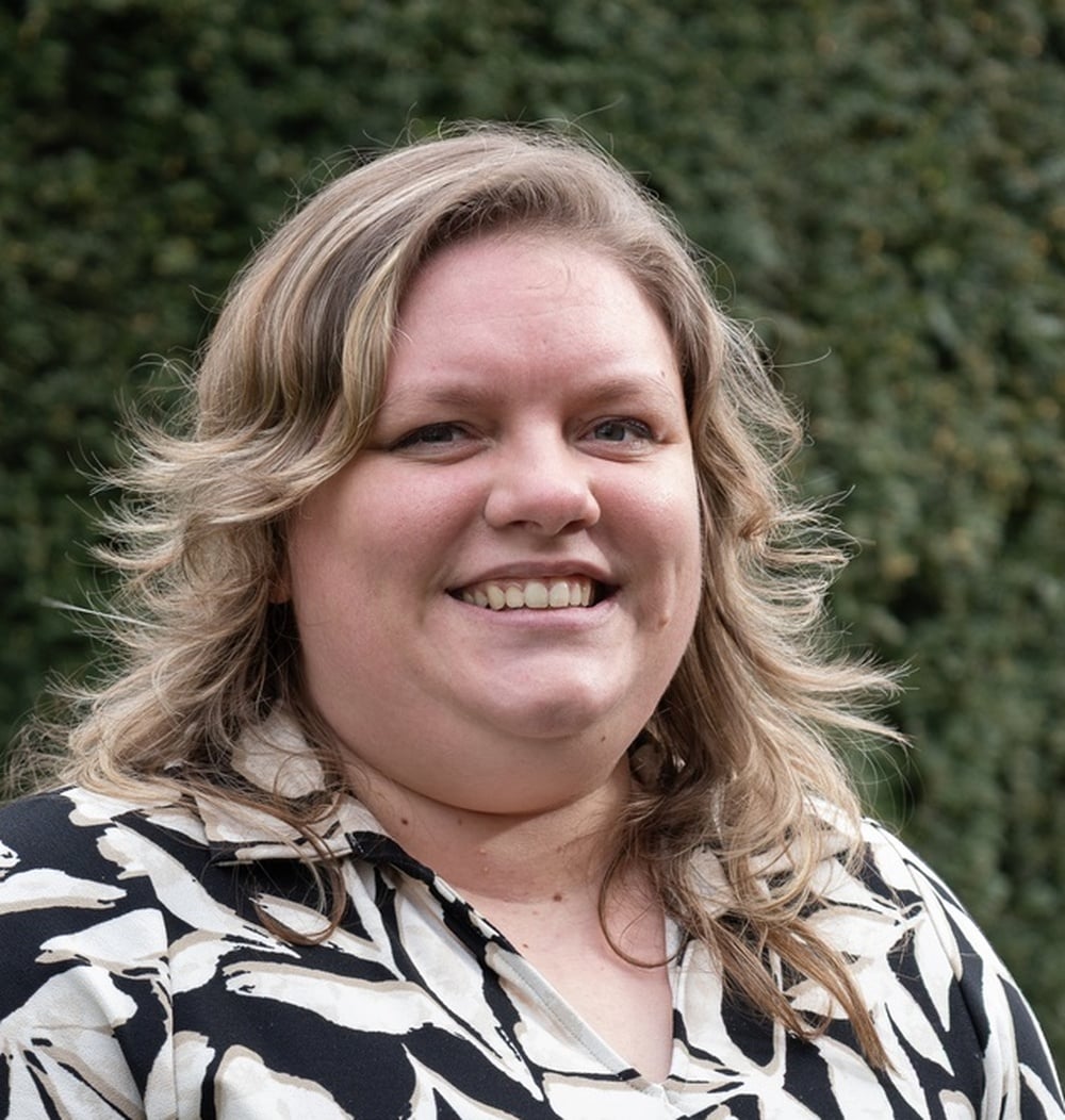 Medewerker van idverde poseert lachend voor een groene heg.