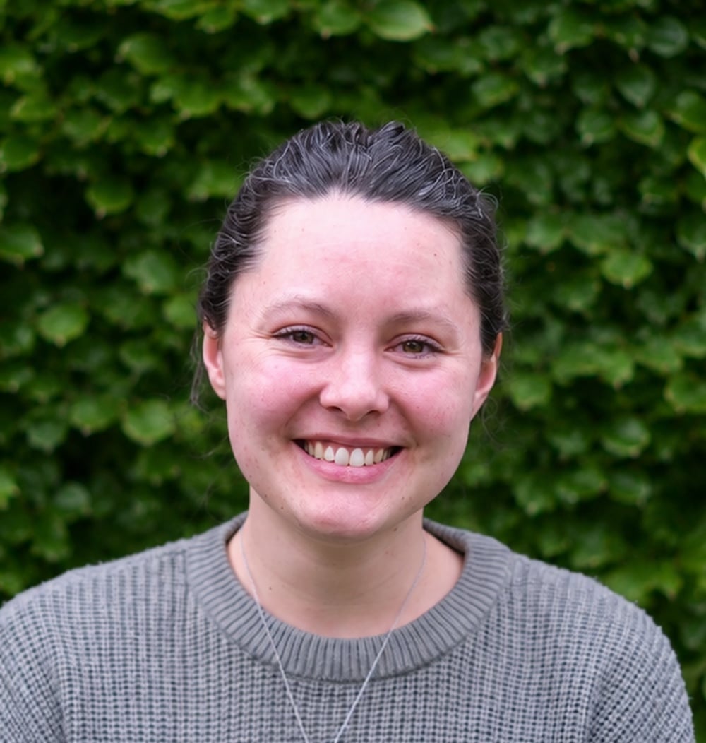 Eline Weenink, GIS-specialist bij idverde, lachend voor een groene heg.