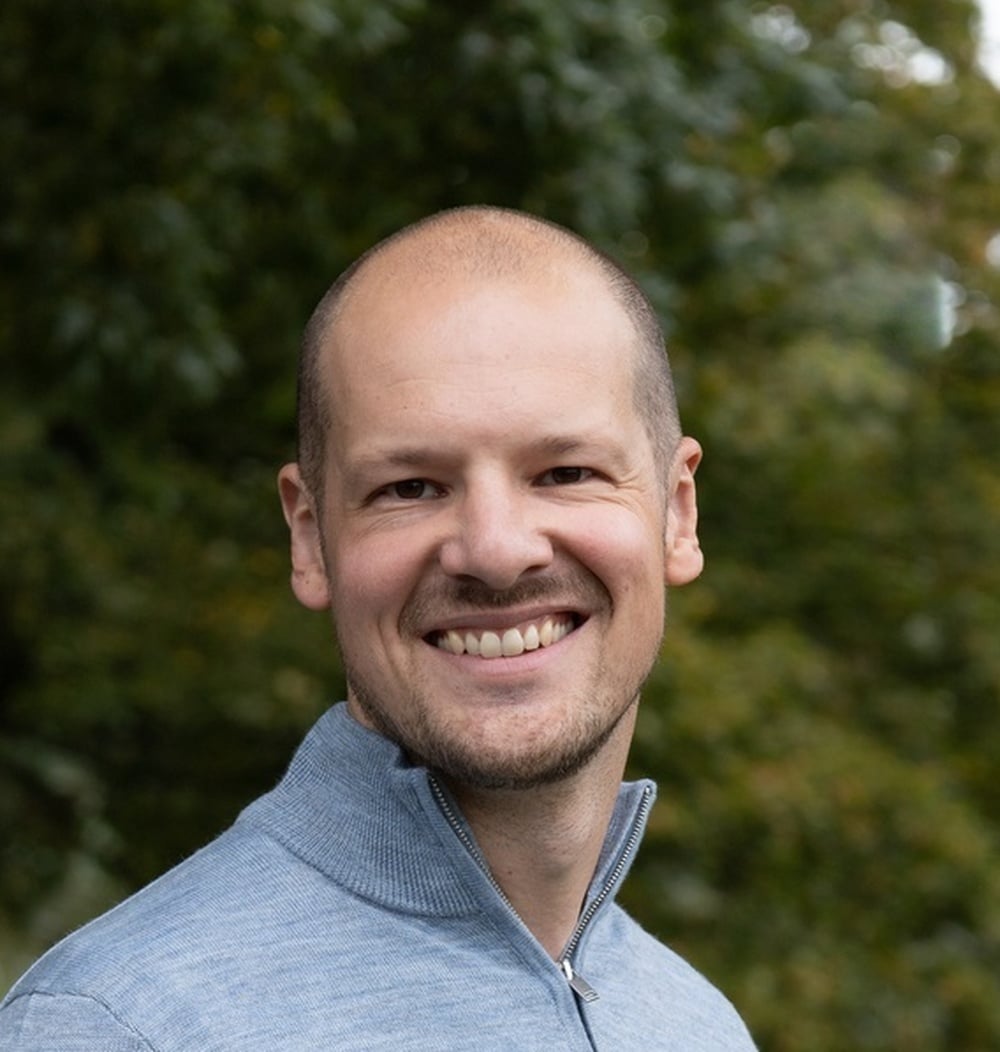 Portret van Elwin Kok, projectleider bij idverde, buiten met groene bomen op de achtergrond.