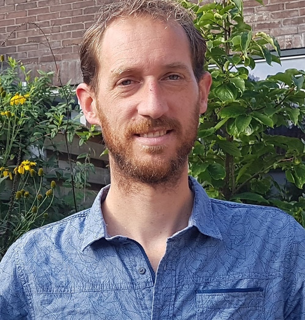 Erik Poorterman, adviseur Spelen bij idverde, glimlachend voor groene beplanting in een tuin.