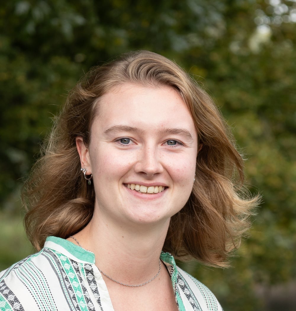 Eva Fletcher, adviseur Strategie & Beleid bij idverde, glimlacht op een portretfoto met groen op de achtergrond.