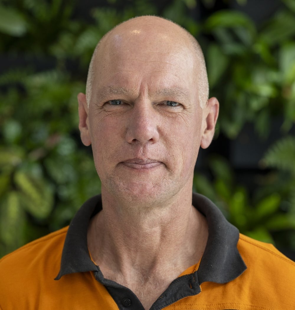 Medewerker in oranje werkpolo poseert voor een groene plantenwand.