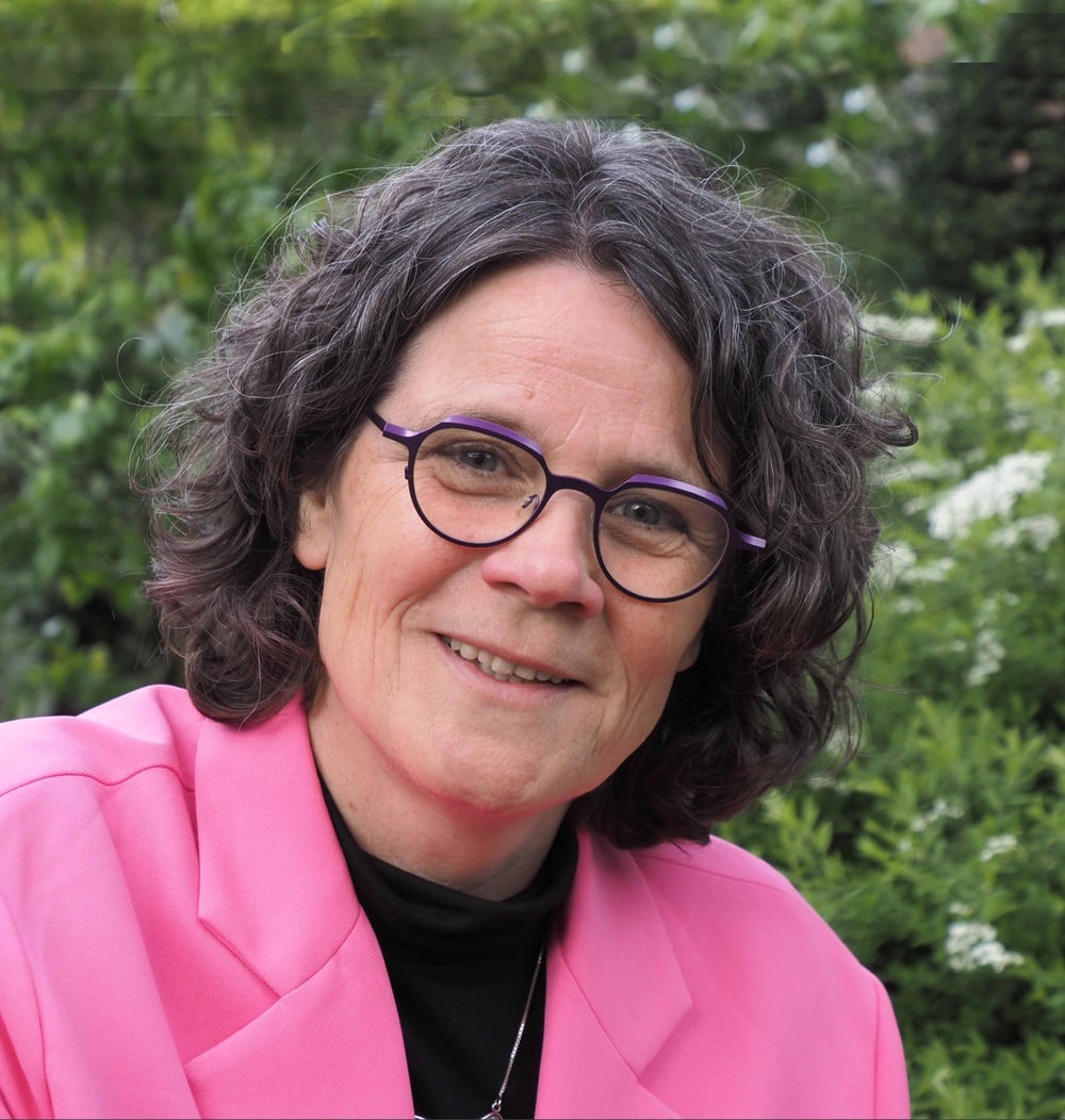 Gerda Kos, projectleider bij idverde, glimlachend voor groene beplanting.