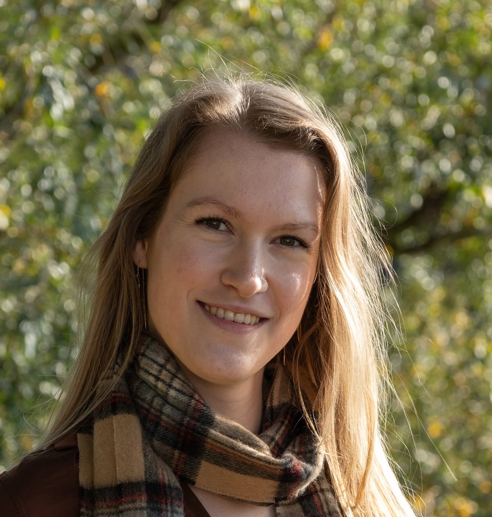 Ilse Kamps, adviseur ecologie bij idverde, lachend voor de camera met bomen op de achtergrond.