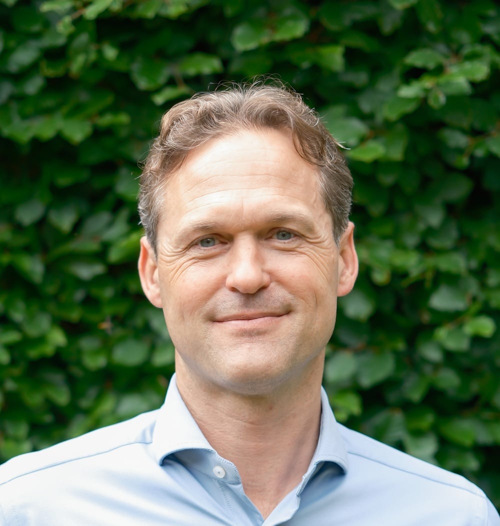 Portretfoto van Joost Heemskerk, CEO, met een groene heg als achtergrond; hij draagt een lichtblauw overhemd.