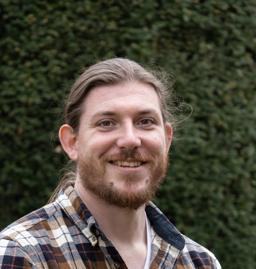 Jorrick Kalter, boomtechnisch adviseur bij idverde, glimlacht voor een groene heg.