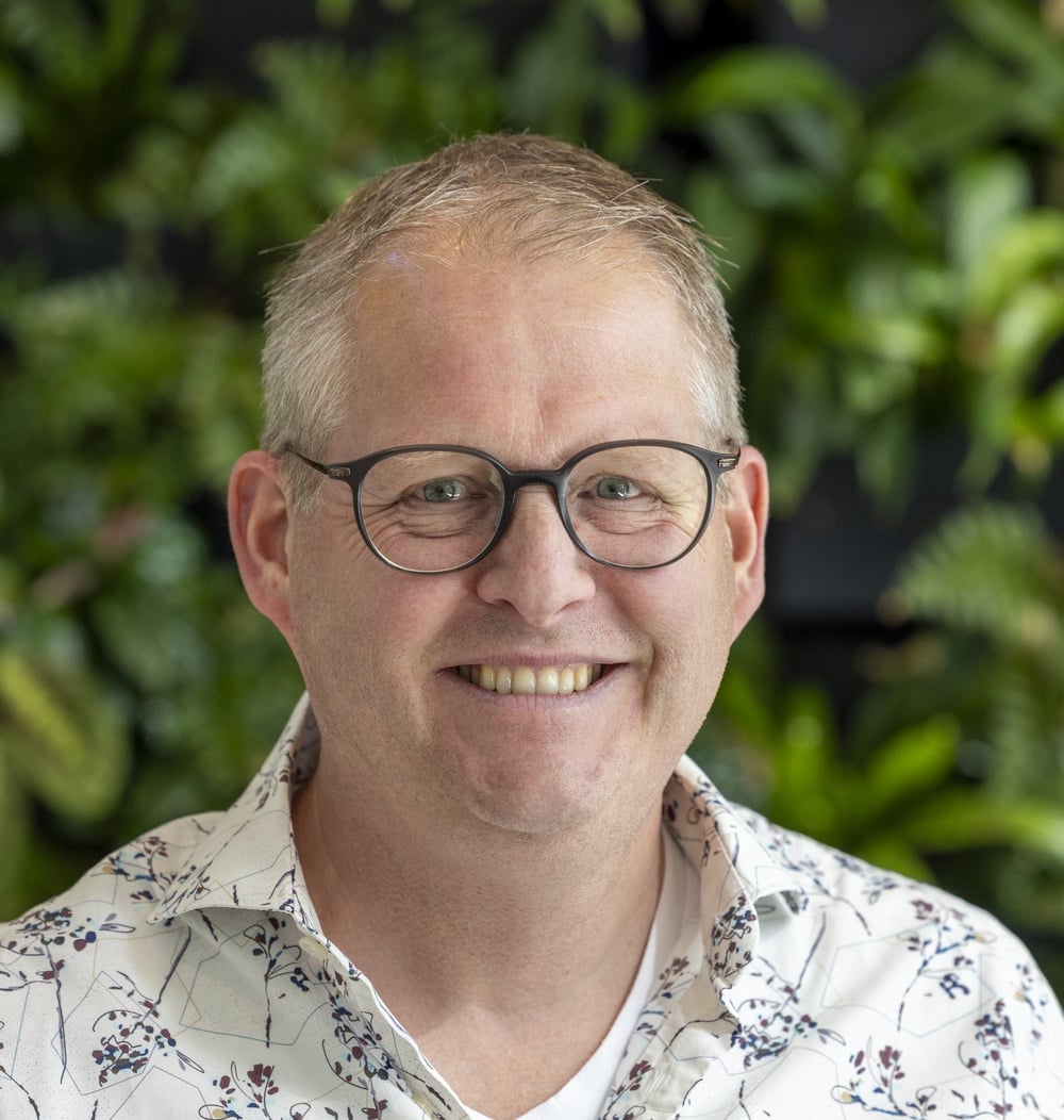 Portret van Marc Lansink, vestigingsmanager, tegen een groene plantenachtergrond.
