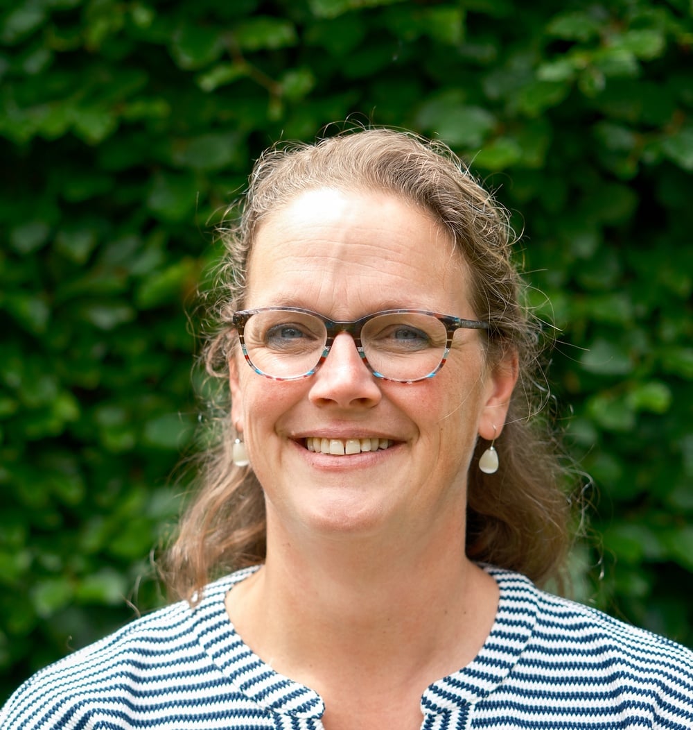 Marjolein Gelen-Wiggers, boomtechnisch adviseur bij idverde, lachend voor een groene heg.
