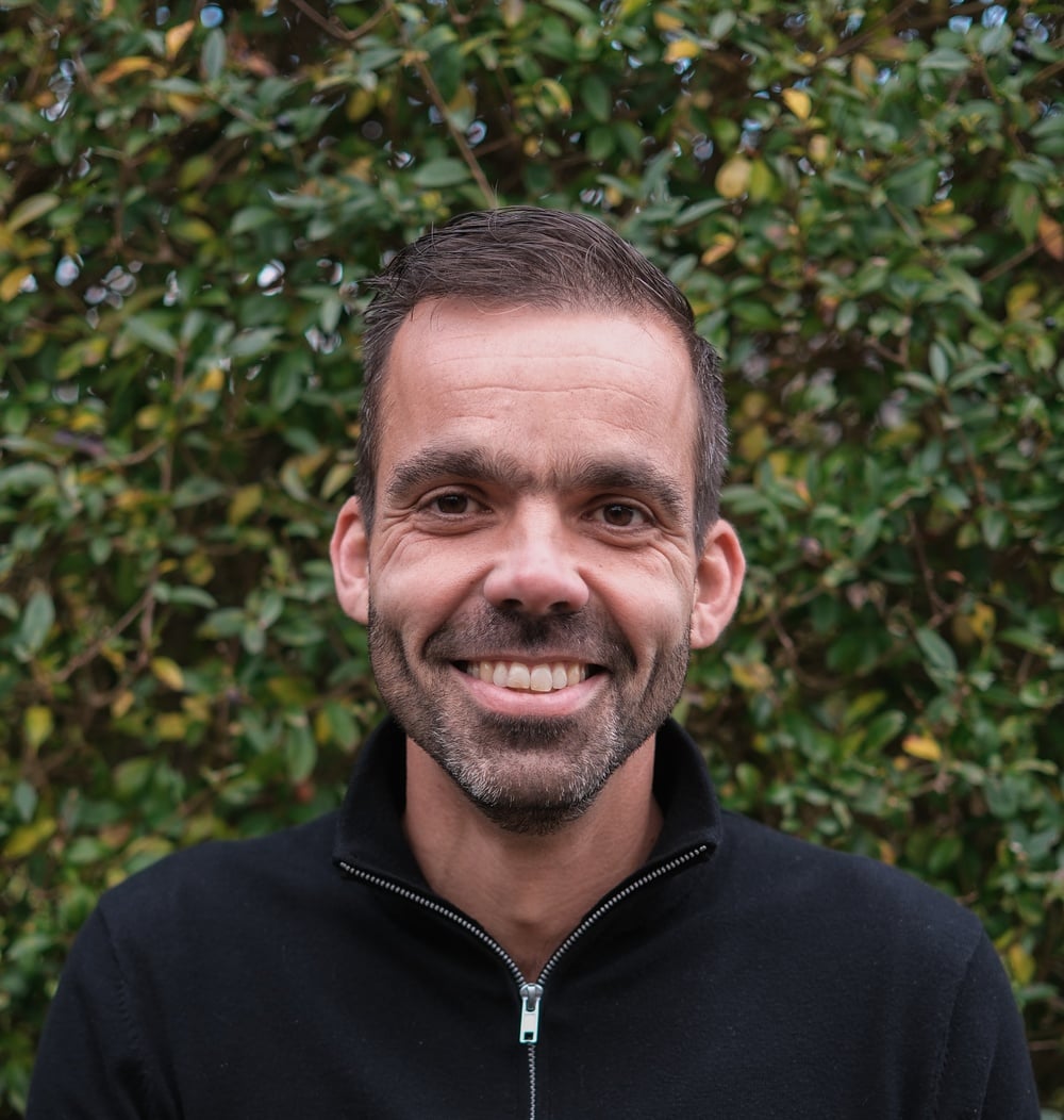 Roland van Braak, regiomanager Zuidwest bij idverde, lachend voor een groene heg.