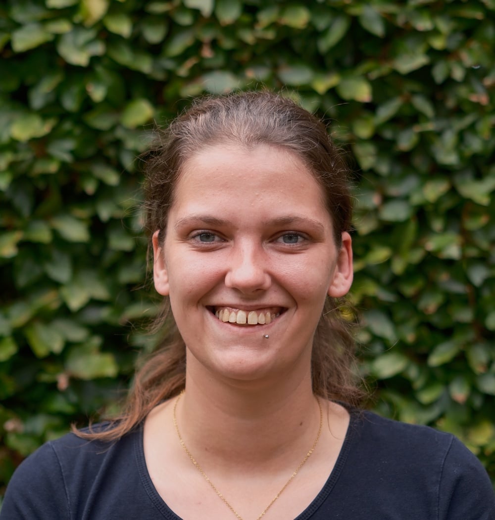 Portret van Samantha Vetjens, werkvoorbereider i.o. bij idverde, voor een groene heg.