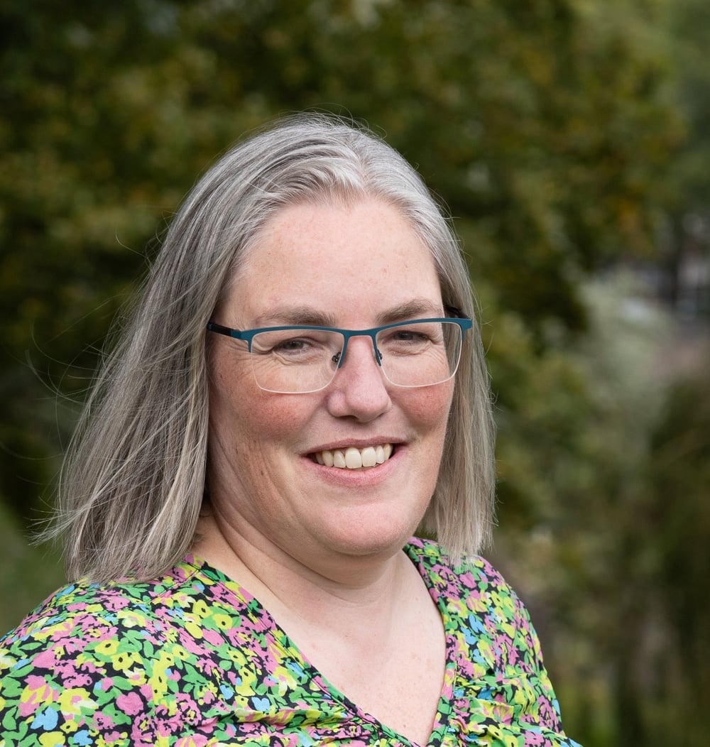 Sandra de Haan, adviseur Ontwerp & Inrichting bij idverde, glimlachend voor groene bomen.