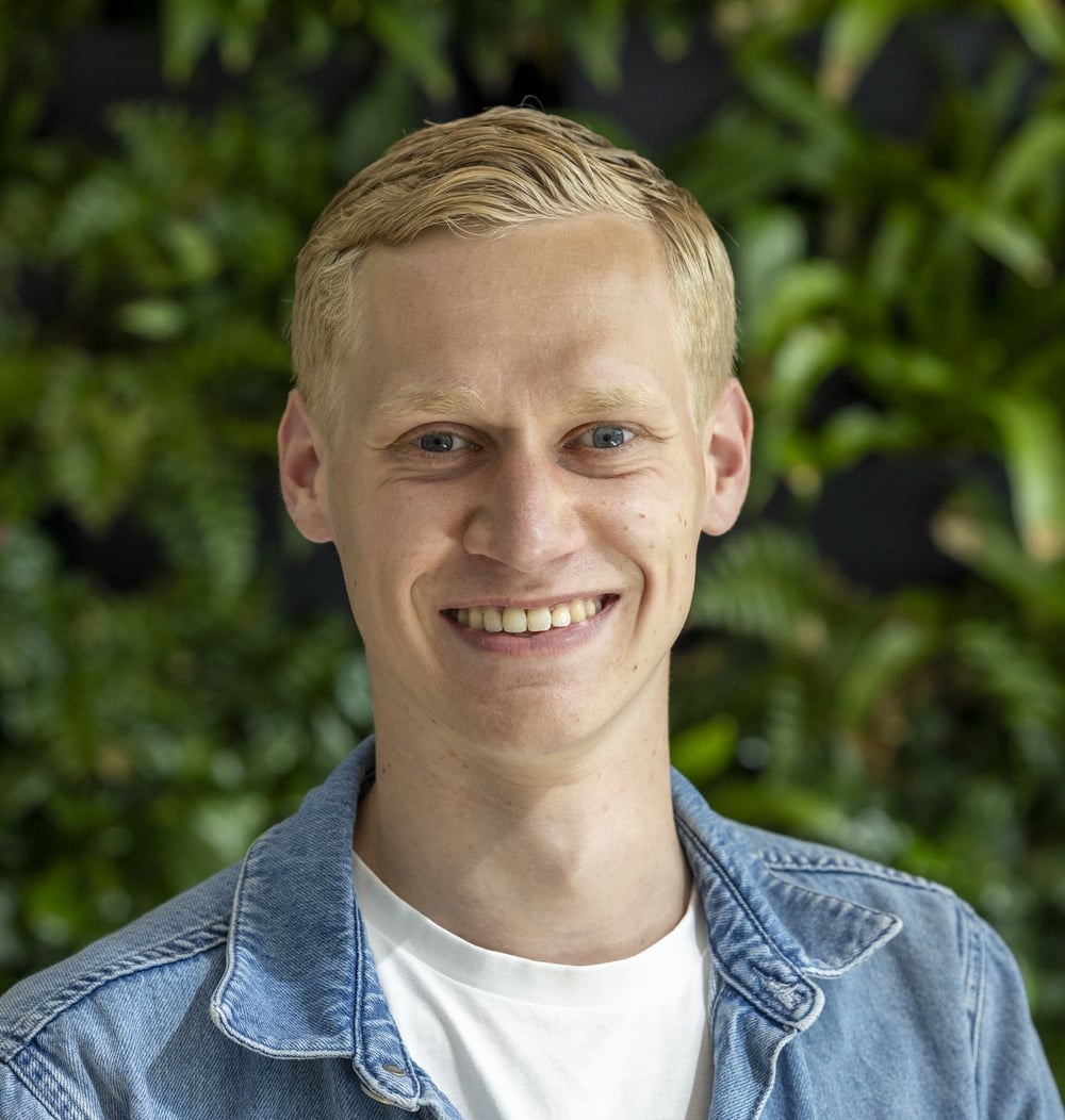 Medewerker van idverde poseert lachend voor een groene plantenwand.