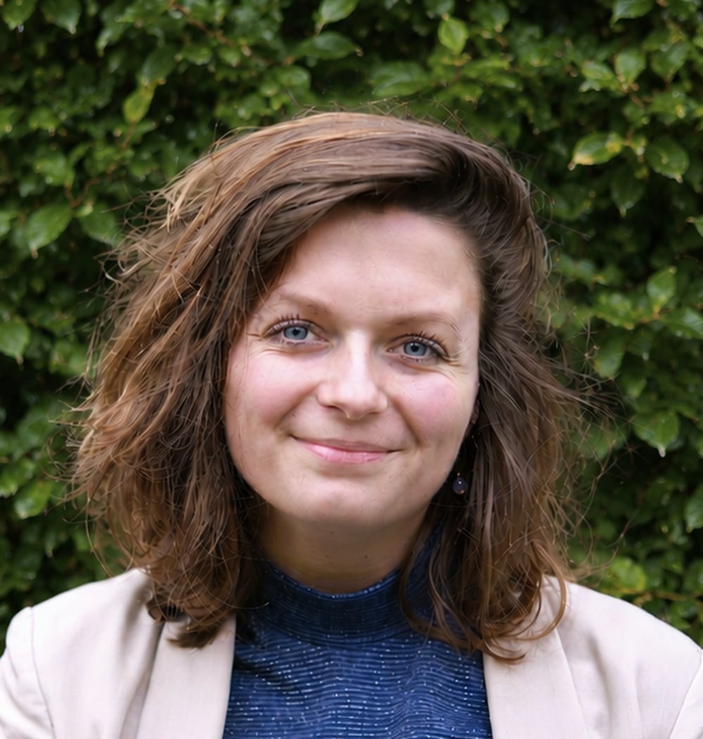 Portretfoto van Yneke van Iersel, adviseur Geo-informatie bij idverde, voor een groene heg.