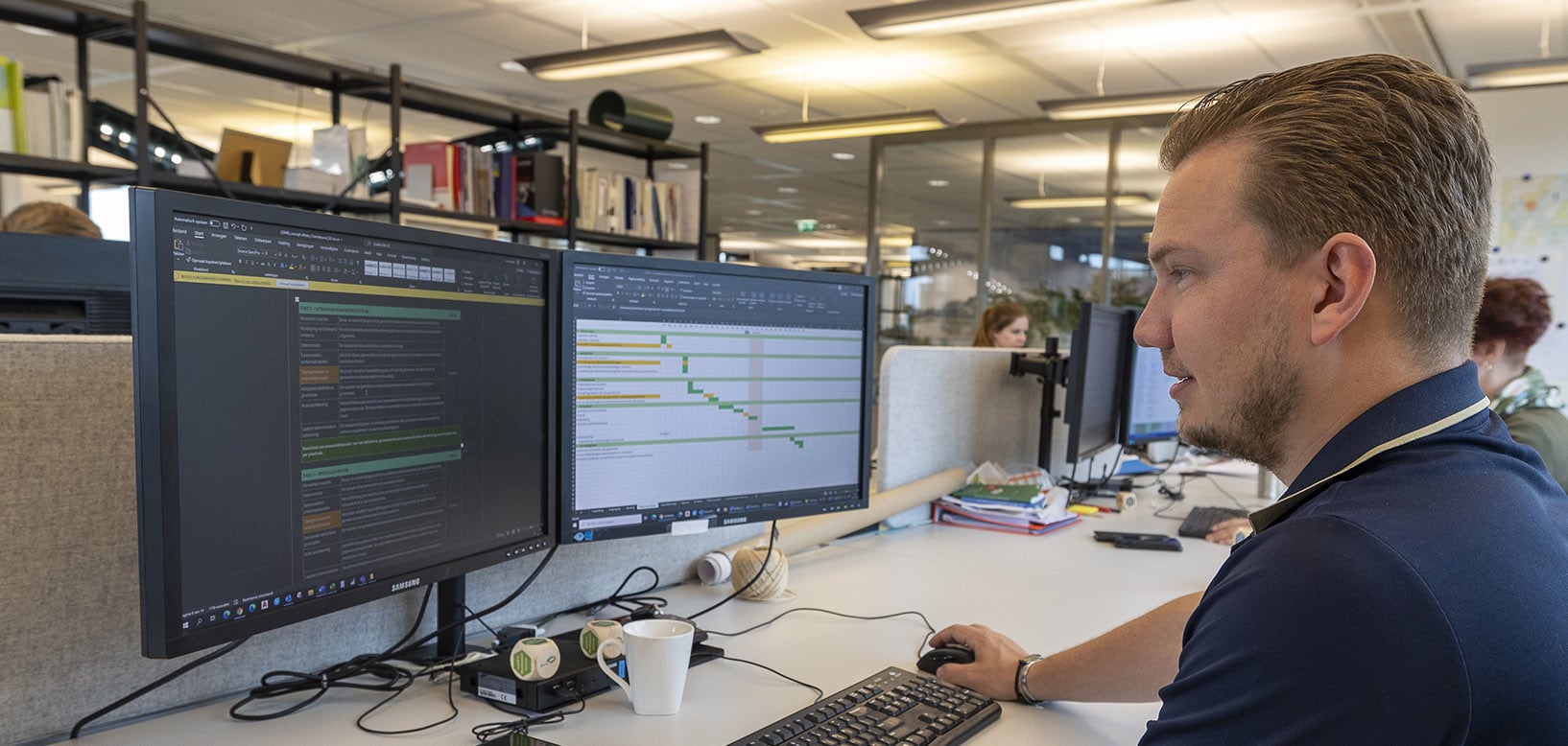 Medewerker van idverde plant projectwerkzaamheden achter een dubbel beeldscherm op kantoor.