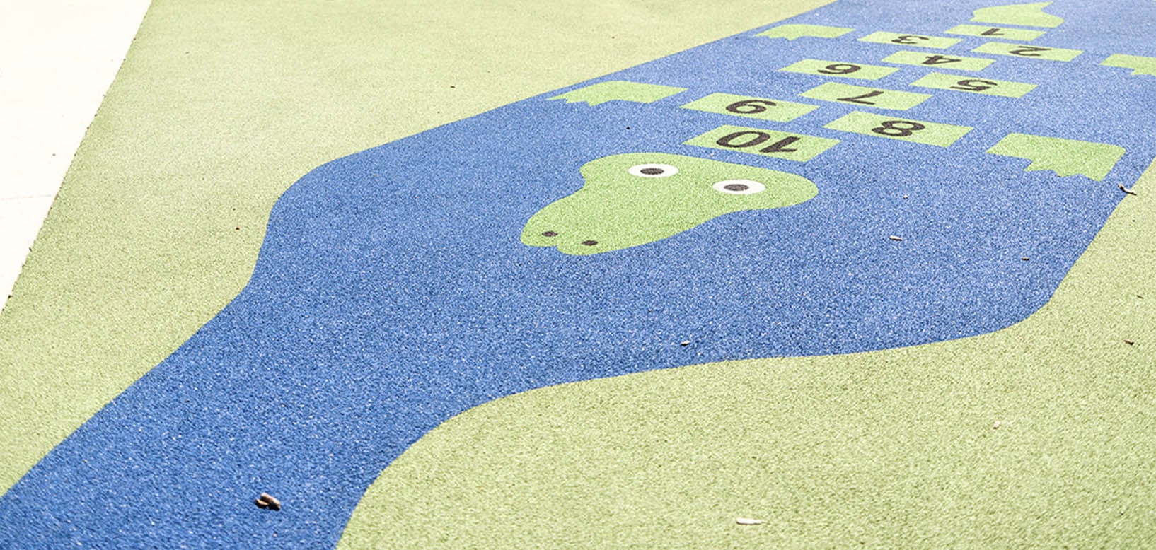 Rubberen valondergrond van speelplaats met blauw-groen motief en hinkelspel met cijfers.