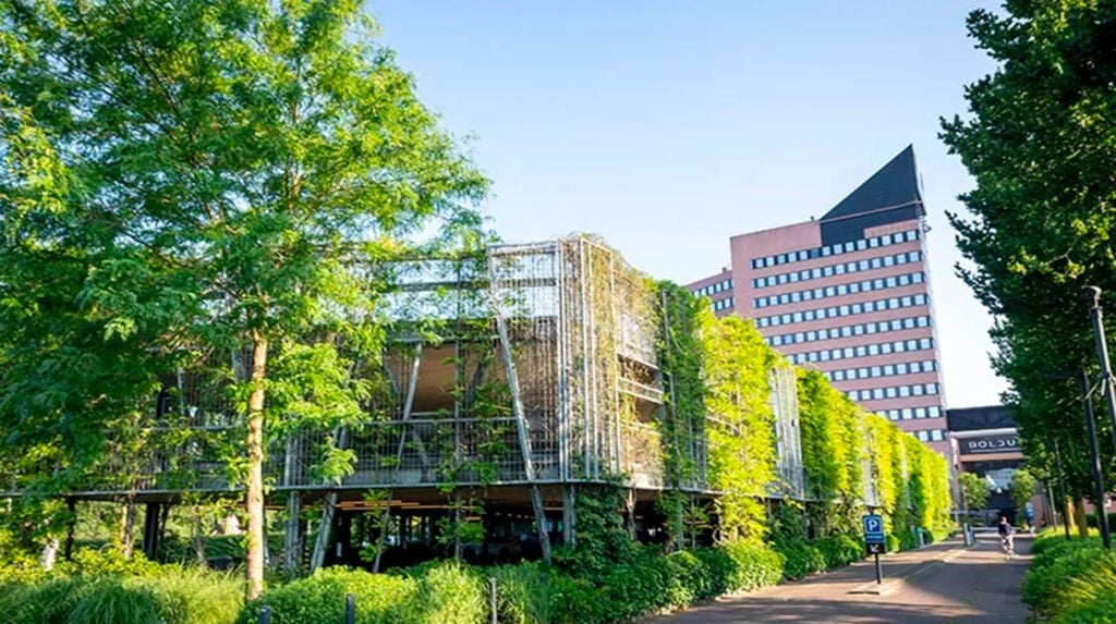 Groen bedrijventerrein met begroeide parkeergarage en kantoorgebouw omringd door bomen en klimplanten