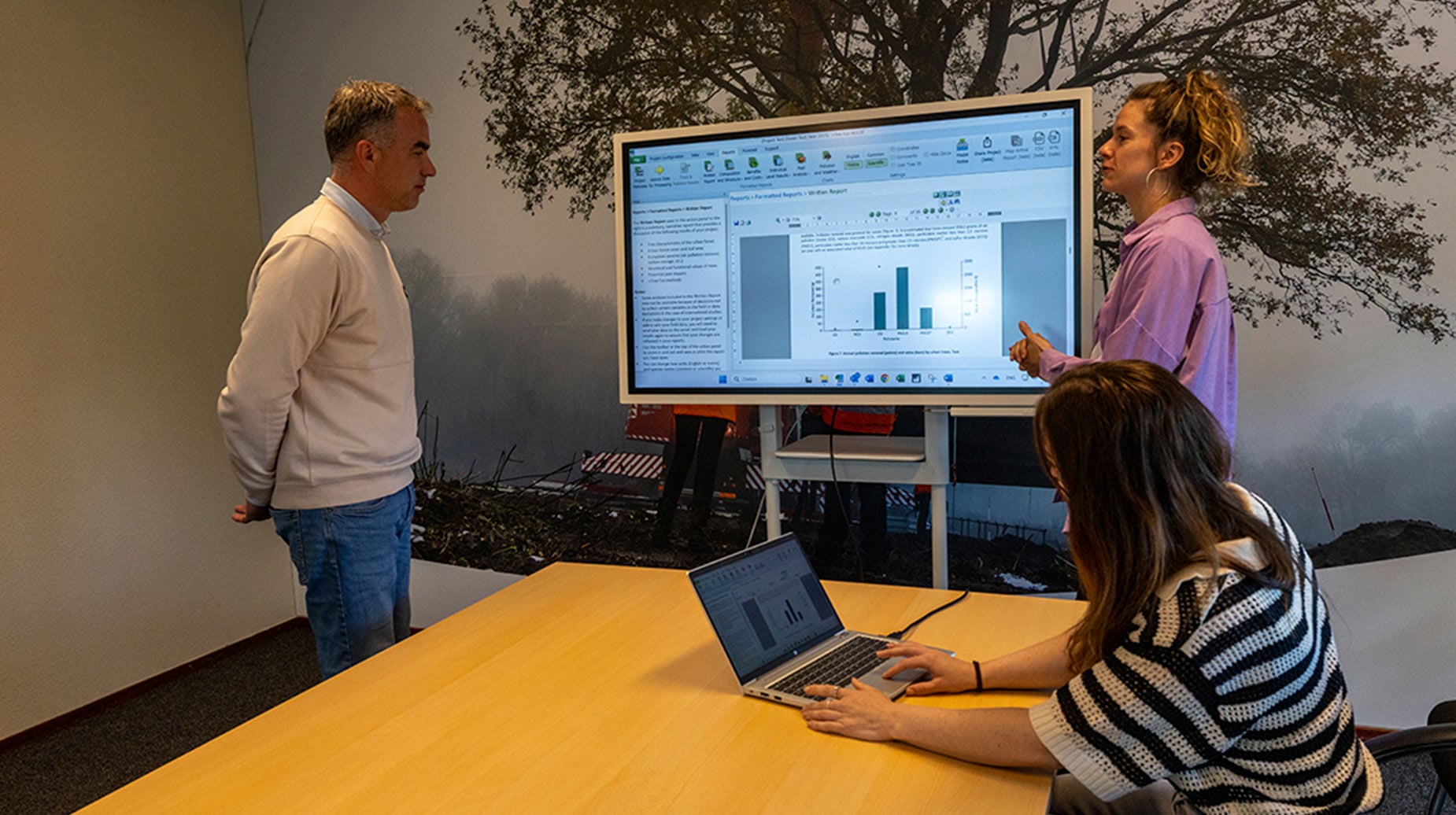 Medewerkers bespreken projectrapportage en data over stedelijk groen op een groot beeldscherm in een vergaderruimte.