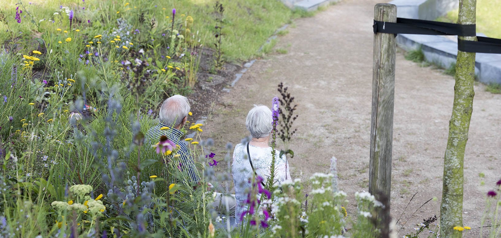 Ouder echtpaar loopt langs een bloemrijke border met wilde bloemen naast een grindpad.