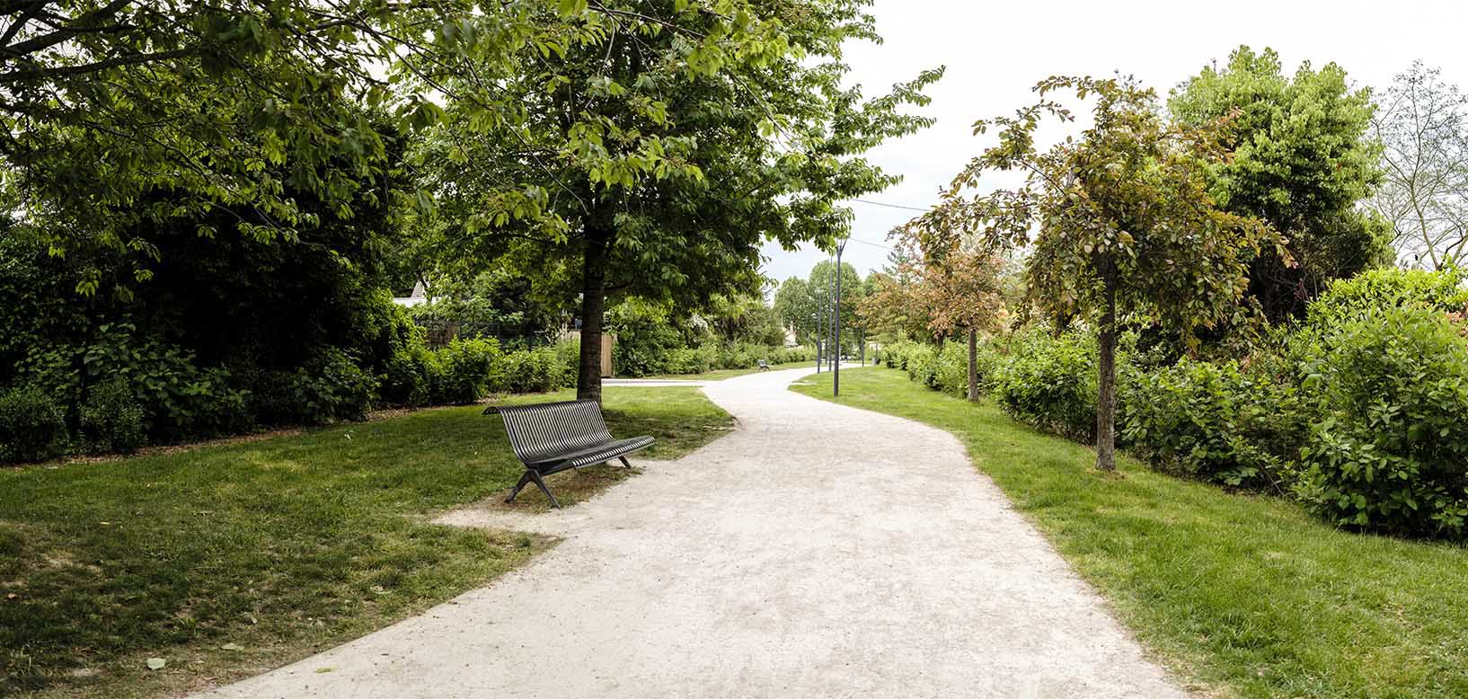 Onderhouden wandelpad met bankje door groenstrook met bomen, gazon en heesters.