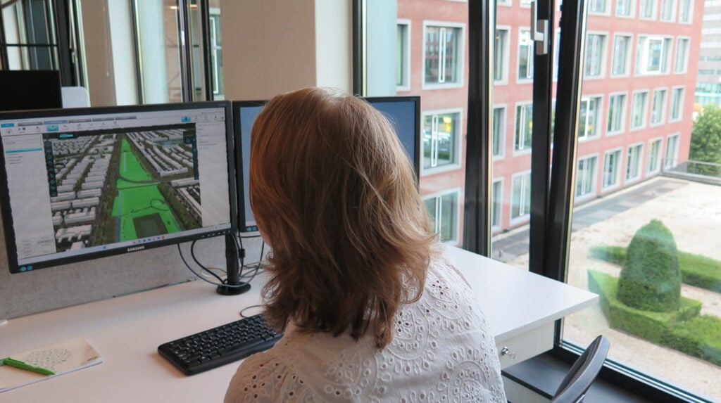 Medewerker analyseert luchtfoto en groenplanning van een woonwijk op een computerscherm op kantoor.