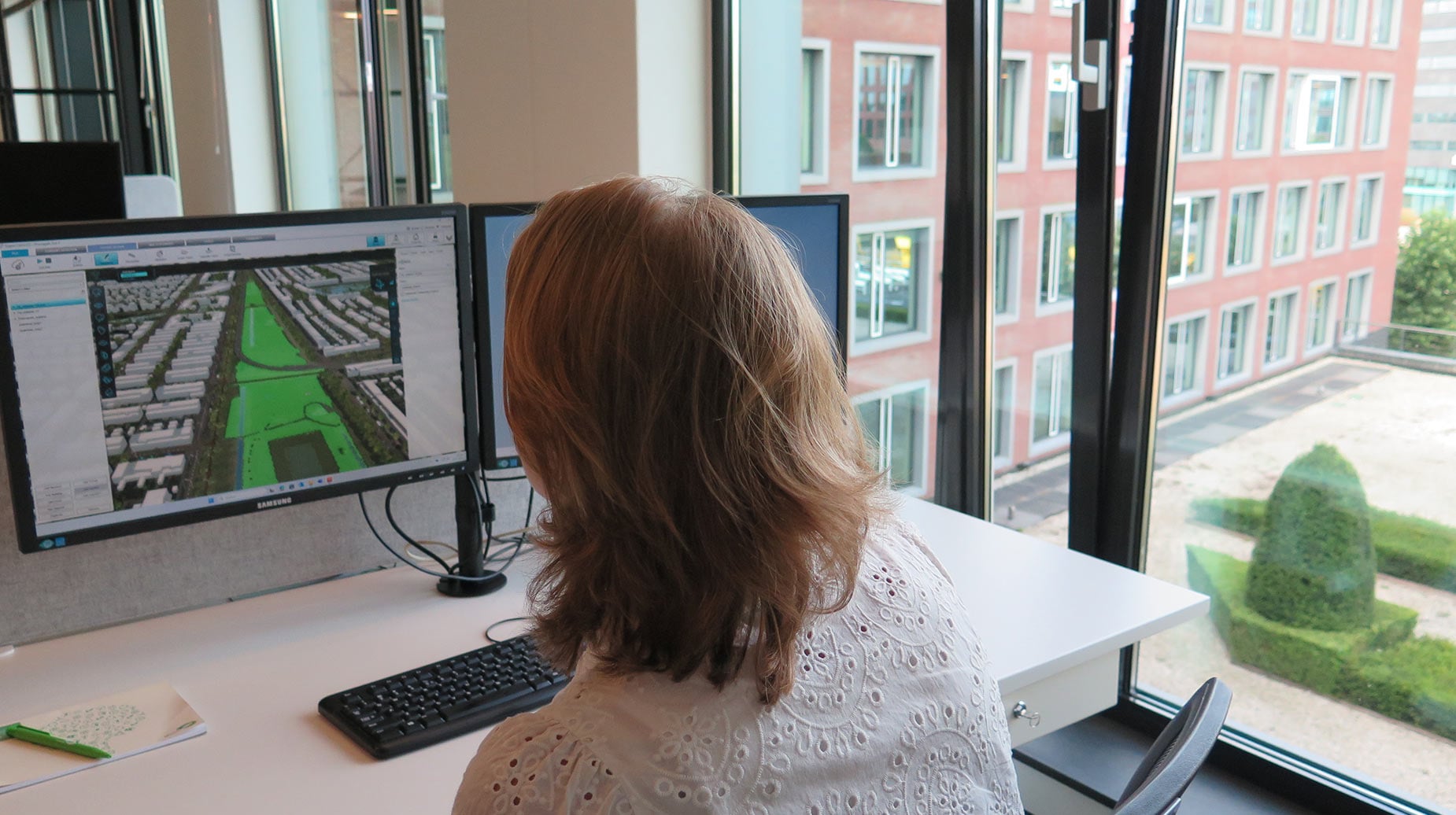 Medewerker analyseert luchtfoto en groenplanning van een woonwijk op een computerscherm op kantoor.
